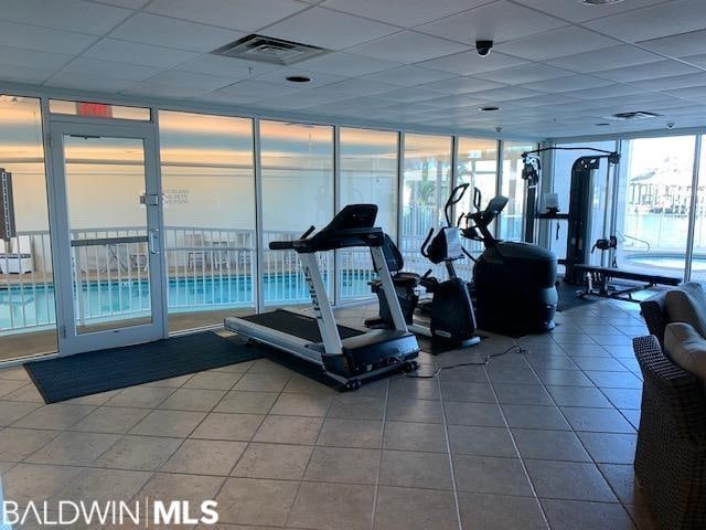 gym featuring a wall of windows, a paneled ceiling, and dark tile flooring