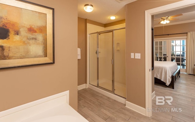 ensuite bathroom with baseboards, ornamental molding, wood finished floors, a textured ceiling, and a shower stall