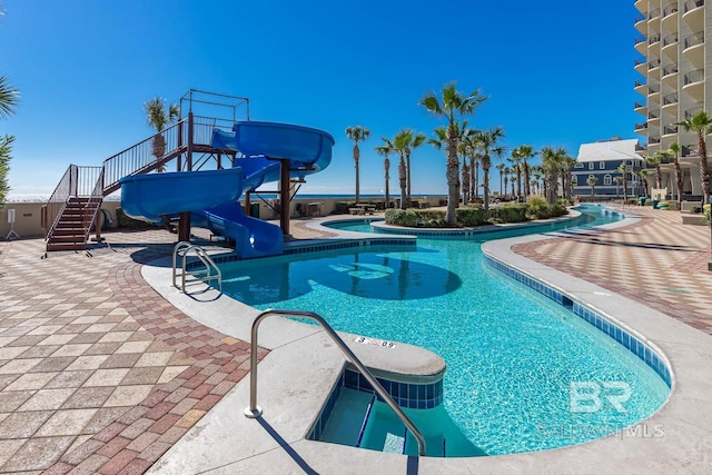 pool featuring a patio area, a jacuzzi, stairs, and a water slide