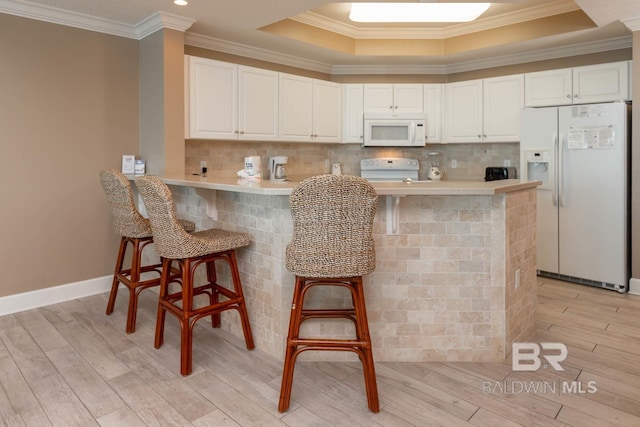 kitchen with white appliances, light wood-style flooring, decorative backsplash, and a kitchen breakfast bar