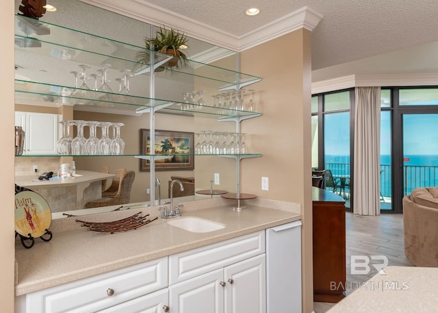 bar featuring a textured ceiling, wood finished floors, a sink, ornamental molding, and indoor wet bar