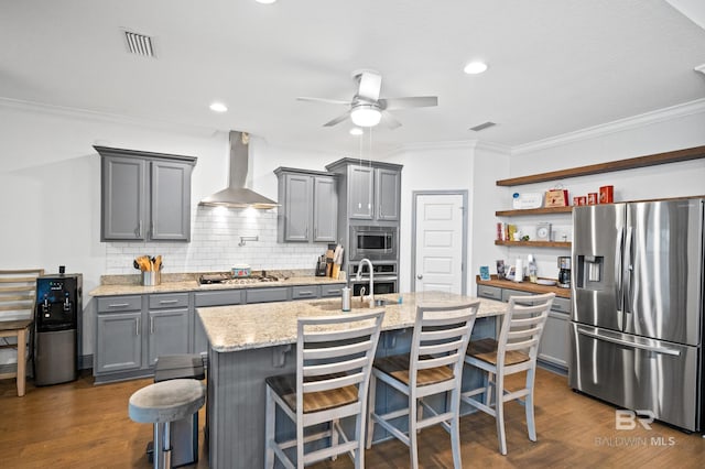 kitchen with sink, a center island with sink, stainless steel appliances, a kitchen bar, and wall chimney exhaust hood