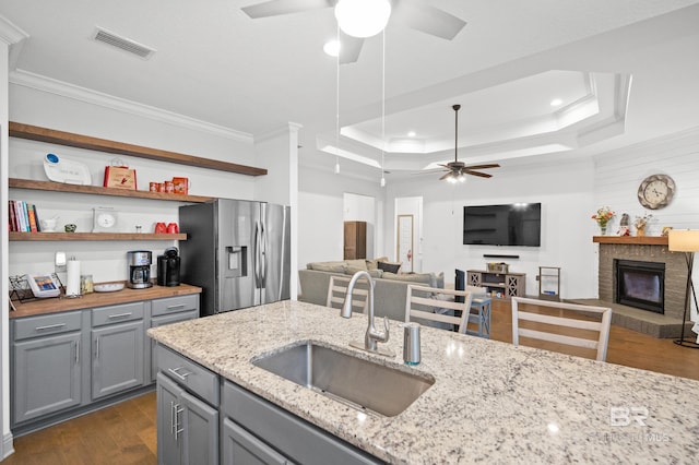 kitchen featuring a raised ceiling, sink, light stone counters, and stainless steel fridge with ice dispenser