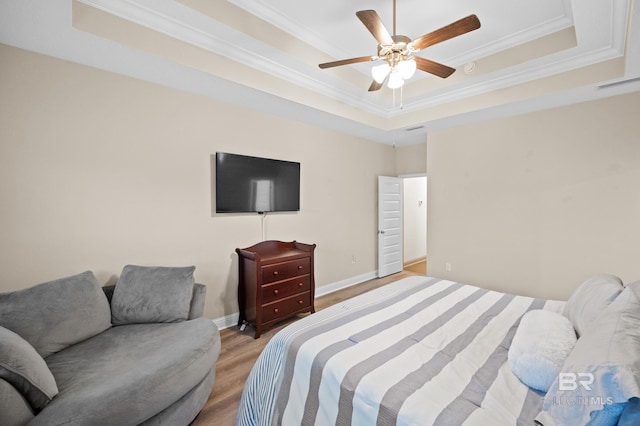 bedroom with ceiling fan, ornamental molding, a tray ceiling, and light wood-type flooring