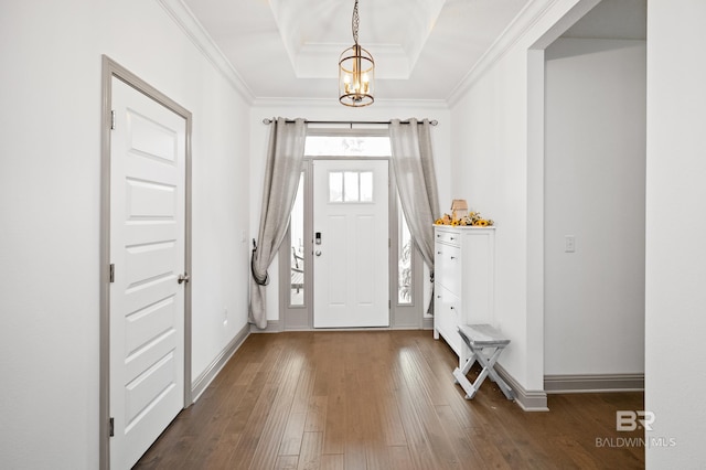 entrance foyer with an inviting chandelier, ornamental molding, a tray ceiling, and dark hardwood / wood-style floors