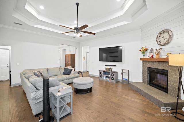 living room featuring wood-type flooring, ornamental molding, ceiling fan, a raised ceiling, and a brick fireplace