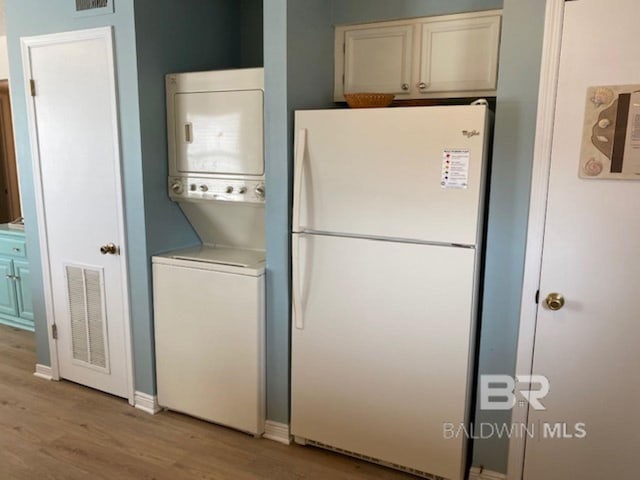 laundry room with stacked washer and dryer and light hardwood / wood-style flooring