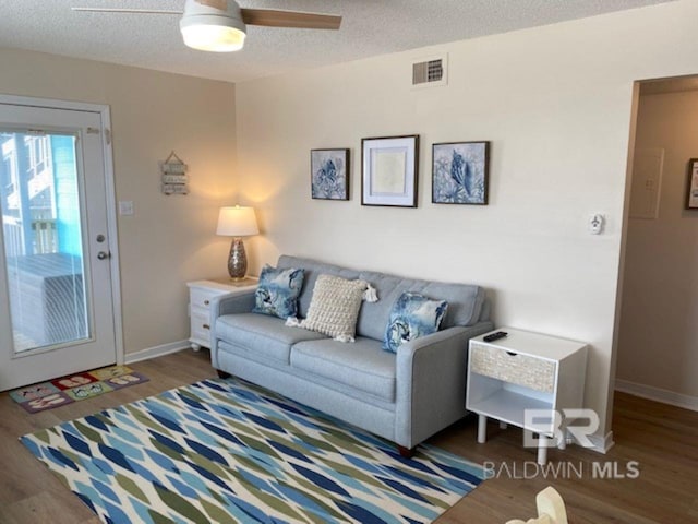 living room featuring dark wood-type flooring, ceiling fan, and a textured ceiling