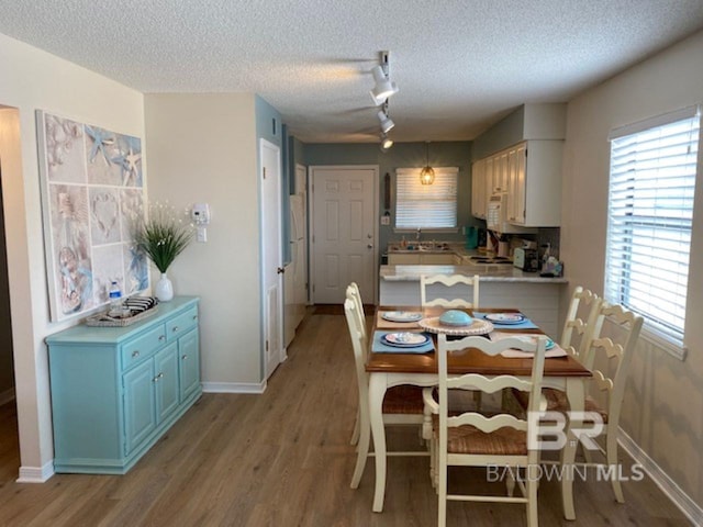 dining room featuring sink, track lighting, a textured ceiling, and light hardwood / wood-style flooring