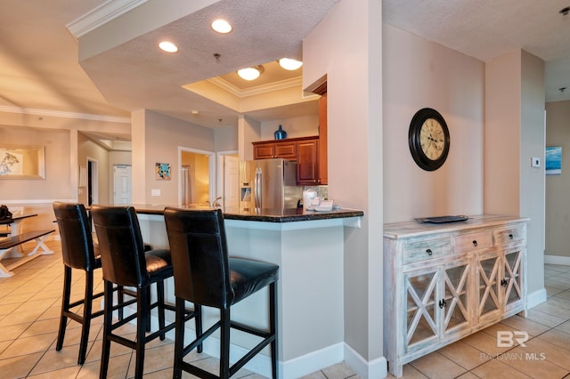 kitchen featuring stainless steel fridge, ornamental molding, a breakfast bar, a textured ceiling, and light tile patterned flooring