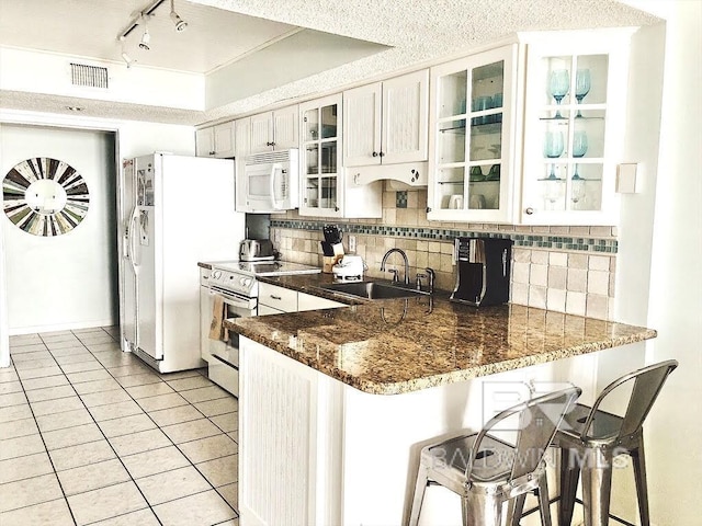 kitchen featuring a peninsula, white appliances, a sink, visible vents, and backsplash