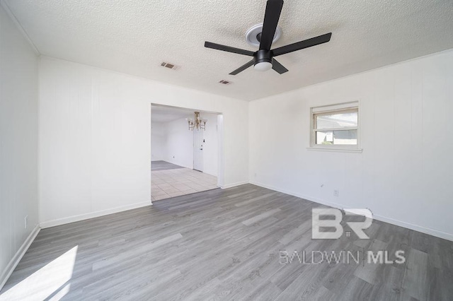 spare room with a textured ceiling, ceiling fan with notable chandelier, wood finished floors, and visible vents