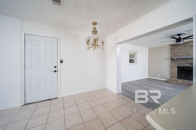 entrance foyer with a textured ceiling, light tile patterned flooring, a brick fireplace, visible vents, and ceiling fan with notable chandelier