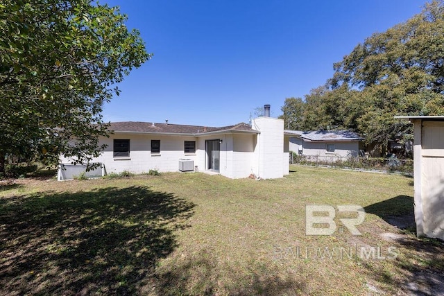 rear view of property with central AC, concrete block siding, and a lawn