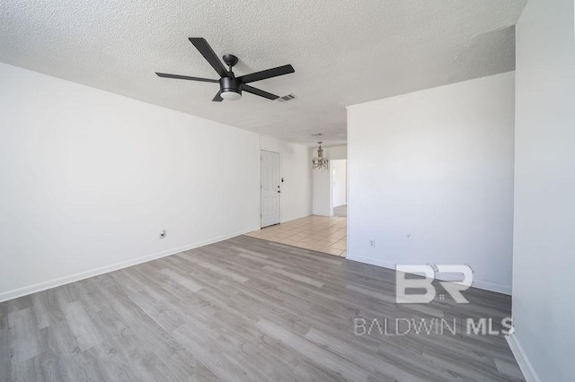 empty room featuring ceiling fan with notable chandelier, a textured ceiling, visible vents, wood finished floors, and baseboards