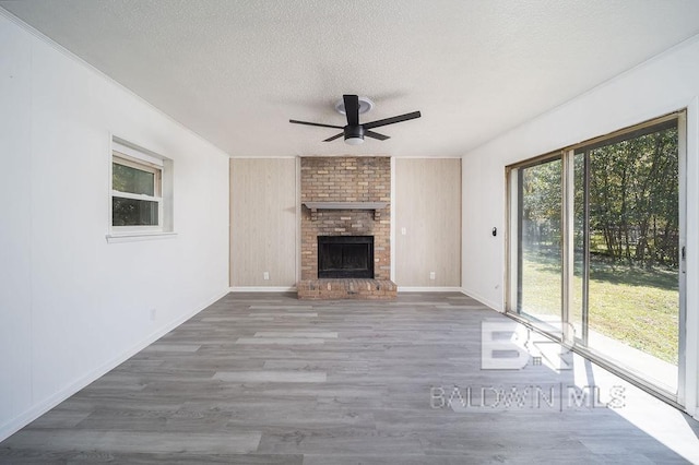 unfurnished living room with a textured ceiling, wood finished floors, a ceiling fan, and a brick fireplace