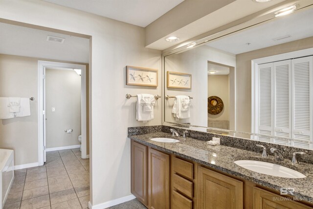 bathroom with a tub, tile patterned flooring, toilet, and dual bowl vanity