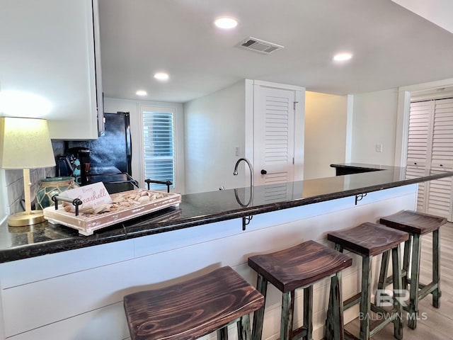 kitchen with dark stone counters, a kitchen bar, black refrigerator, tasteful backsplash, and kitchen peninsula