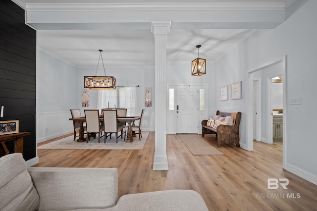 living area with baseboards, light wood finished floors, an inviting chandelier, decorative columns, and ornamental molding