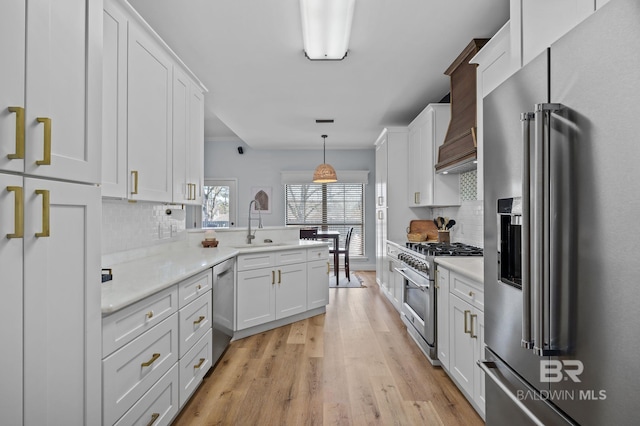 kitchen featuring high end appliances, light wood-style flooring, a sink, light countertops, and white cabinetry