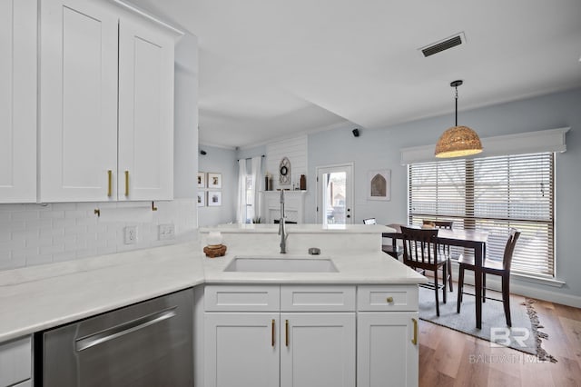 kitchen with visible vents, a sink, a peninsula, white cabinets, and dishwasher