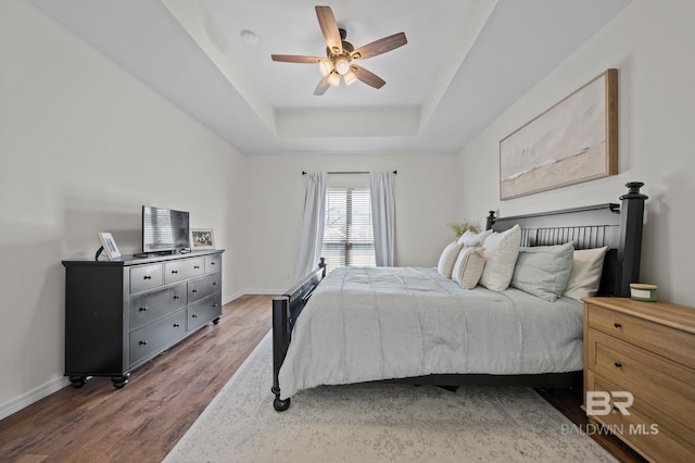 bedroom featuring ceiling fan, baseboards, a raised ceiling, and wood finished floors