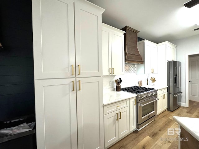 kitchen with backsplash, light countertops, premium appliances, light wood-style floors, and custom exhaust hood