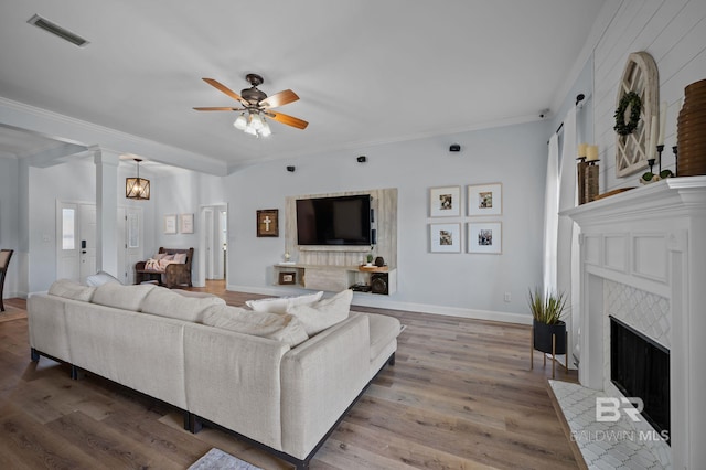 living area with visible vents, ornamental molding, a ceiling fan, wood finished floors, and a fireplace