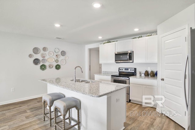 kitchen with stainless steel appliances, sink, light hardwood / wood-style floors, white cabinetry, and an island with sink