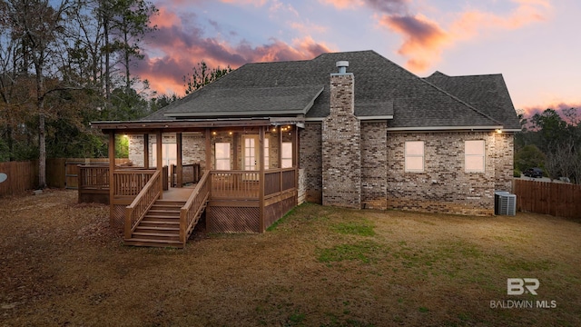 back house at dusk with a wooden deck, central AC, and a lawn