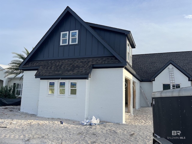 view of side of home with brick siding, board and batten siding, and roof with shingles