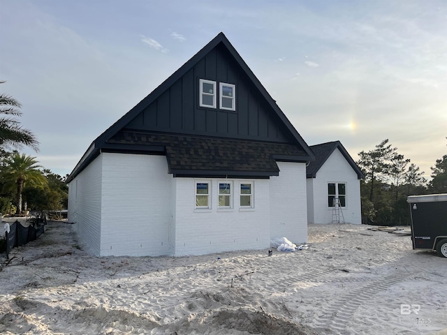 back of property featuring board and batten siding, roof with shingles, and brick siding