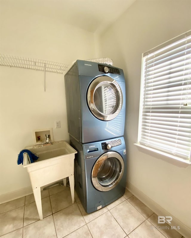 laundry area with stacked washer / drying machine and light tile patterned floors