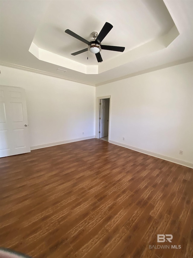 spare room with dark wood-type flooring, ceiling fan, and a raised ceiling