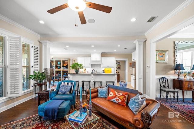 living room with decorative columns, ceiling fan, dark hardwood / wood-style floors, and crown molding