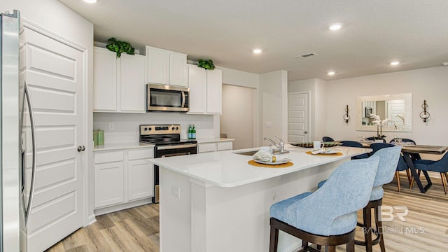 1040 Hayward Loop, Foley, AL 36535 - kitchen featuring appliances with stainless steel finishes, light wood finished floors, an island with sink, a breakfast bar area, and white cabinets