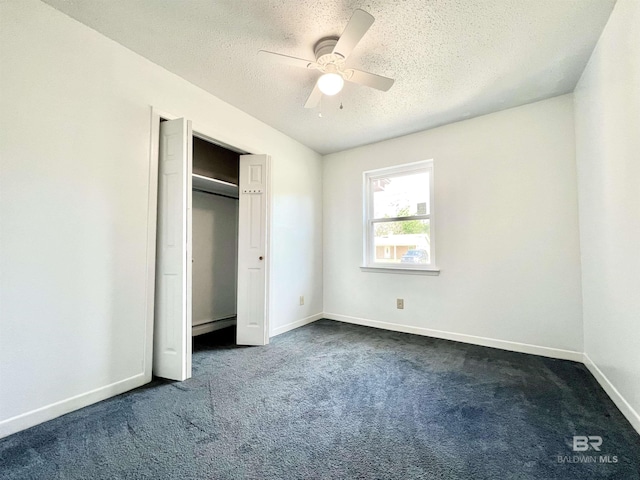 unfurnished bedroom with a closet, baseboards, dark colored carpet, ceiling fan, and a textured ceiling