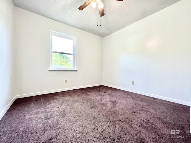 unfurnished room with baseboards, dark carpet, and a ceiling fan