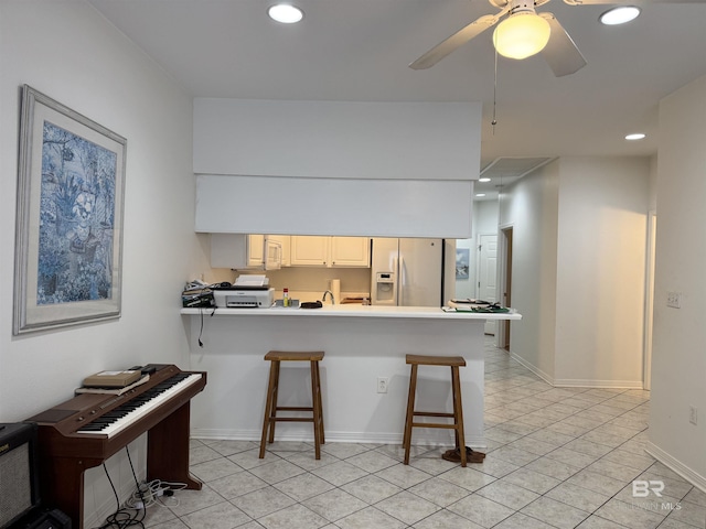 kitchen with a kitchen bar, kitchen peninsula, ceiling fan, refrigerator with ice dispenser, and white cabinetry