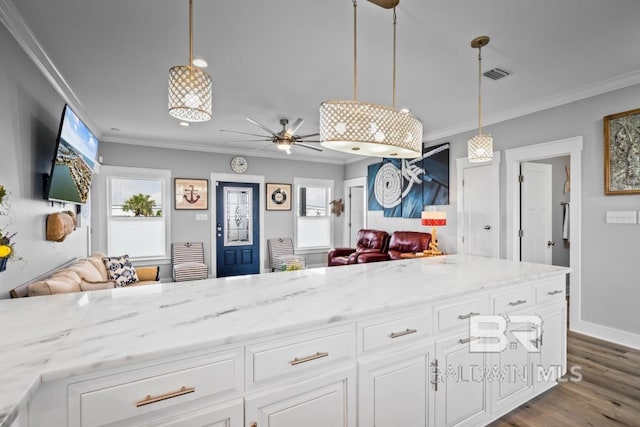 kitchen with white cabinetry, crown molding, light stone counters, and decorative light fixtures