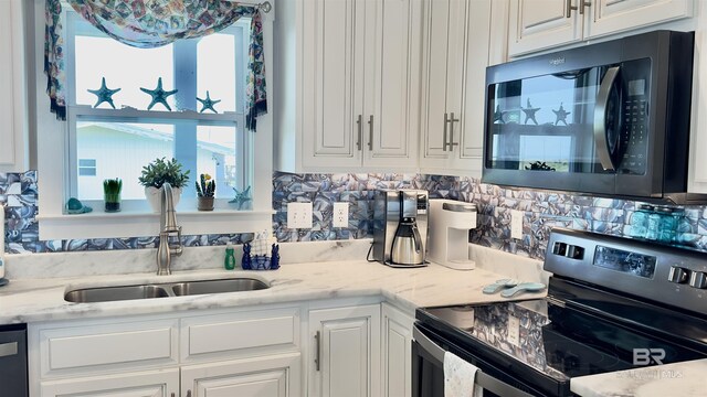 kitchen featuring white cabinets, backsplash, light stone countertops, appliances with stainless steel finishes, and sink