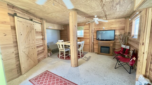 basement featuring wooden ceiling, wood walls, a barn door, and ceiling fan