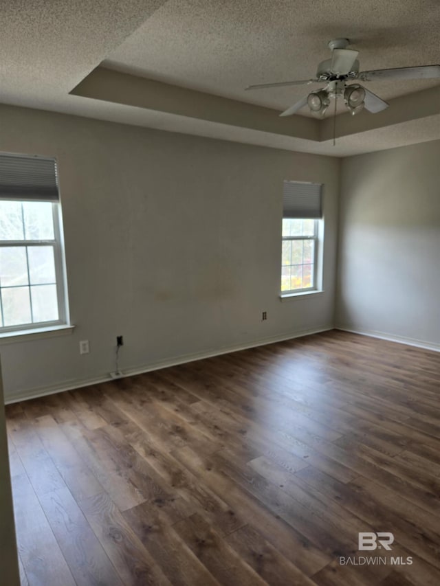 unfurnished room featuring a textured ceiling, a tray ceiling, dark wood-style flooring, and baseboards