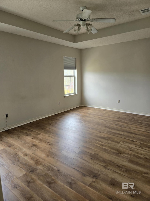 empty room with a textured ceiling, dark wood finished floors, visible vents, and baseboards