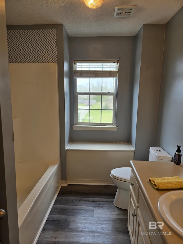 full bath with a textured ceiling, toilet, wood finished floors, vanity, and visible vents