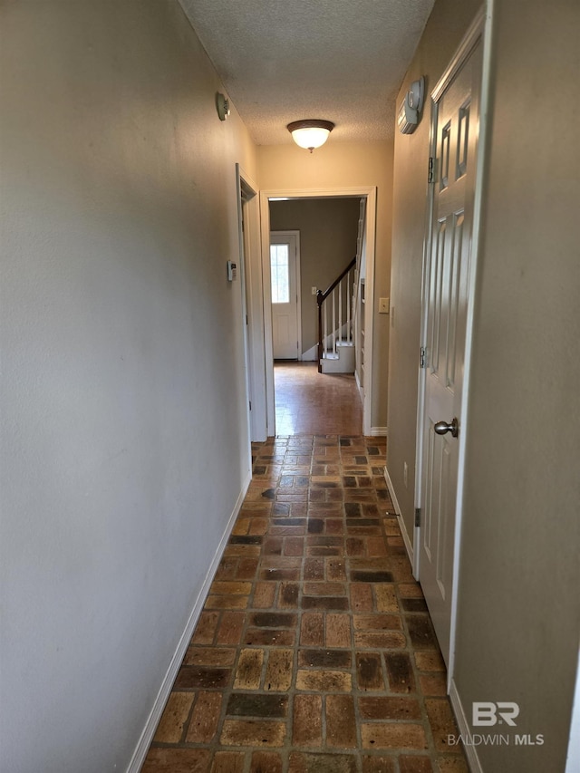 corridor with brick floor, stairway, baseboards, and a textured ceiling