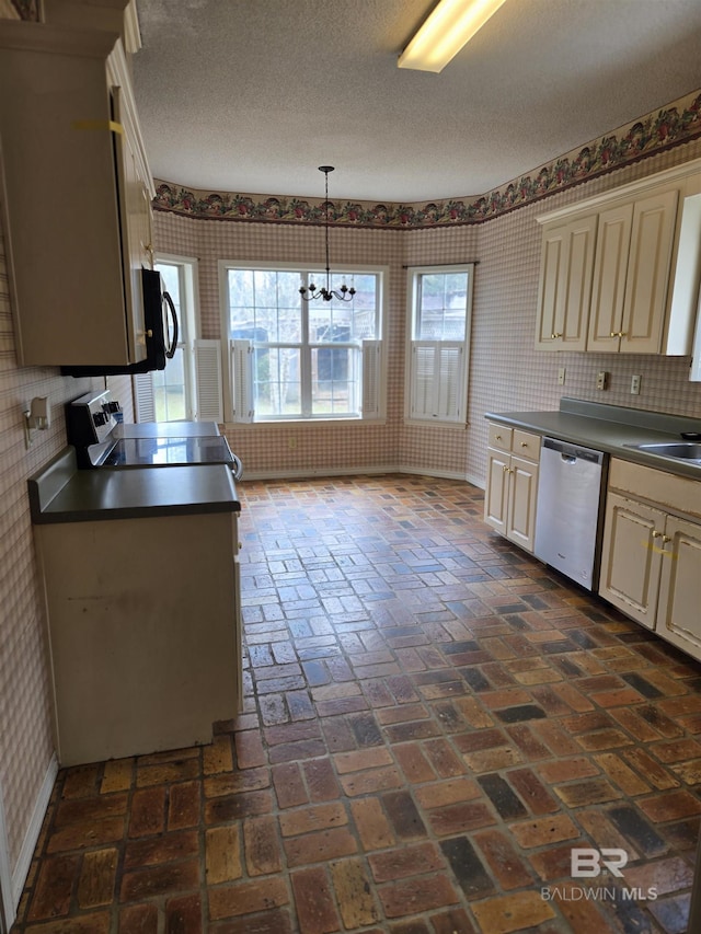 kitchen with stainless steel appliances, cream cabinetry, dark countertops, and wallpapered walls