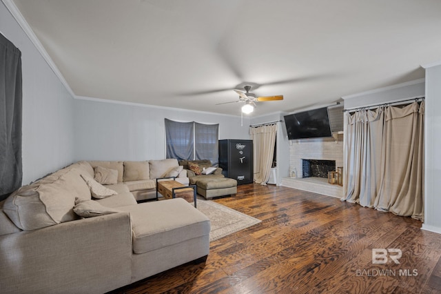 living room featuring ceiling fan, ornamental molding, a large fireplace, and dark wood-type flooring