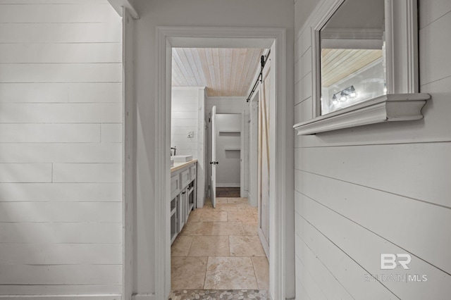 hallway featuring a barn door, stone tile floors, and wood walls