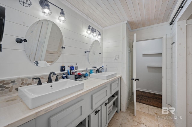 bathroom featuring ornamental molding, wood ceiling, stone finish floors, double vanity, and wood walls